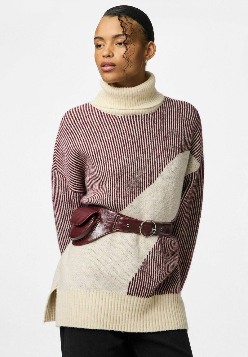 Pletený svetr s vysokým rolákem, sepraný pruhy v barvě kaštanově červené a smetanové. V kombinaci s širokým hnědým páskem, který dodává strukturovaný akcent. Černé kalhoty.