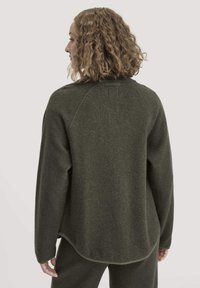 Maglione in pile verde oliva con finitura testurizzata, maniche raglan e orlo arrotondato. Presenta un piccolo etichetta sul retro del collo.
