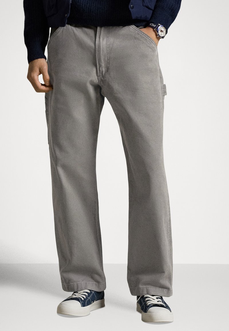 Harmaat puuvillahousut rennolla istuvuudella, joissa on sivutaskut ja sileä pinta. Yhdistetty sinisiin ja valkoisiin nauhallisiin tennareihin.