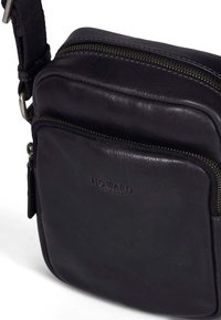 Borsa a tracolla nera in pelle con scomparti con zip, caratterizzata da un logo in rilievo e una tracolla regolabile. Texture liscia, forma rettangolare.