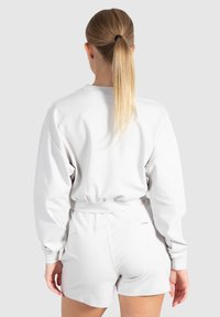 Lichtgrijze sweatshirt met een relaxte pasvorm, verlaagde schouders en elastische zoom; gecombineerd met bijpassende shorts. Gladde, zachte stoftextuur.