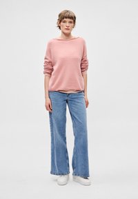 Camisola de malha rosa claro com decote largo, mangas compridas, combinada com jeans de perna larga azul-claro e ténis brancos.