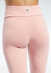 Puha rózsaszín, magasan derekú leggingsek sima textúrával és Reebok logó címkével. A dizájn minimális varrásokat tartalmaz, a letisztult megjelenés érdekében.
