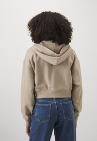 Hoodie beige court avec capuche à cordon et poignets côtelés, associé à un jean en denim bleu taille haute. Tissu lisse et coupe décontractée.