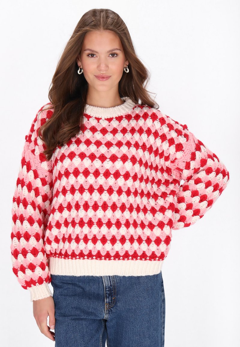 Knit sweater featuring a diamond pattern in red, pink, and cream colors, with a scoop neck and voluminous sleeves. Ribbed cuffs and hem.