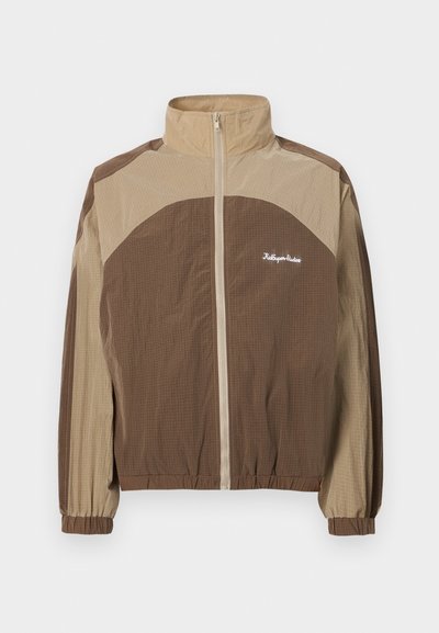 Brown and beige zip-up jacket with a high collar, textured fabric, elastic cuffs, and a logo on the left chest area.
