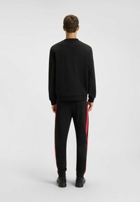 Felpa nera e pantaloni con strisce laterali rosse, realizzati in un tessuto liscio. L'outfit presenta un collo a giro e un design a gamba affusolata.