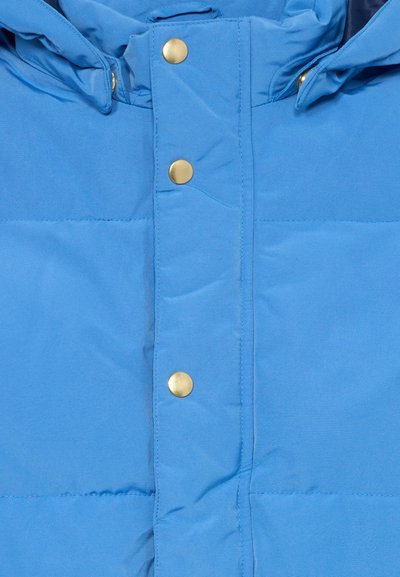 Gaiši zils pūšamais mētelis ar quilted dizainu, ar zelta pogām un regulējamu kapuci. Gluda tekstūra, praktisks un silts.