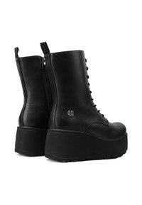 Botas de plataforma de cuero negro con un diseño de cordones, cremallera lateral y una suela de goma gruesa y texturizada. Incluye un acento de logo en el lado exterior.
