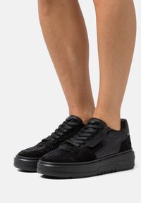 Baskets noires avec une tige en mesh texturé, des accents en daim et une semelle en caoutchouc épaisse. Lacets et détail de marque sur le côté.