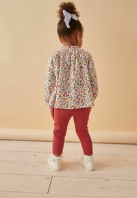 Kleurrijke blouse met bloemenpatroon en elastische halslijn, gecombineerd met roze leggings en witte schoenen met kantafwerking.