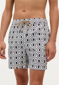 Swim shorts with a navy and white zigzag pattern, elastic waistband, and a beige drawstring. Made of lightweight, smooth material.
