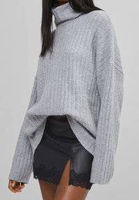 Grå ribbad stickad turtlenecktröja med långa ärmar, med en lös passform och höga sidoflikar, tillsammans med en svart faux läderkjol.