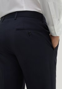 Pantaloni blu con una texture liscia, una tasca laterale e una chiusura a bottone sulla tasca posteriore. Design aderente con una vestibilità sartoriale.