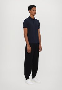 Navy polo shirt with short sleeves paired with black joggers and white sneakers. Simple design, cotton material, minimal branding.