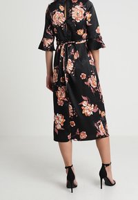 Černé květinové šaty s širokými rukávy, s páskem v oblasti pasu a květinovým vzorem v odstínech růžové a oranžové. Hladká textura podobná saténu.