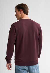 Bordeaux sweatshirt met lange mouwen, een ronde hals, textuurstof en geribde manchetten. De achteraanzicht toont een naadloos schouderontwerp.