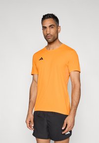 Orangenes, sportliches T-Shirt mit schwarzem Adidas-Logo, kurzen Ärmeln, rundem Ausschnitt und einer leichten, glatten Textur. Kombiniert mit schwarzen Shorts.