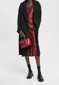 Svart kappa, bärnstensfärgad paljettklänning, röd väska, blanka skor och svarta strumpor. Slät textur och lagerdesign med kontrasterande färger.