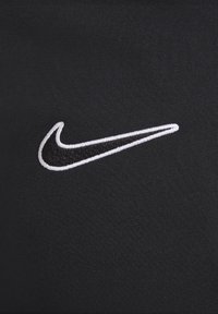 Tissu noir avec un logo Swoosh blanc brodé au centre de la surface, présentant des détails de couture fine sur le design.