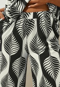 Tela con patrón de hojas en blanco y negro con un acabado texturizado. Los pantalones presentan una cinturilla elástica y un diseño de corte relajado.