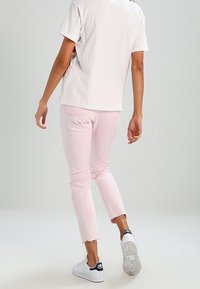 Light pink denim jeans with a cropped, frayed hem. Paired with a loose white t-shirt and white sneakers featuring black accents.