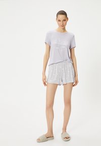 Lys lilla bomulds pyjamas sæt med en T-shirt, der har teksten "Drøm stort" og sky grafik, parret med mønstrede shorts. Blødt, behageligt materiale.