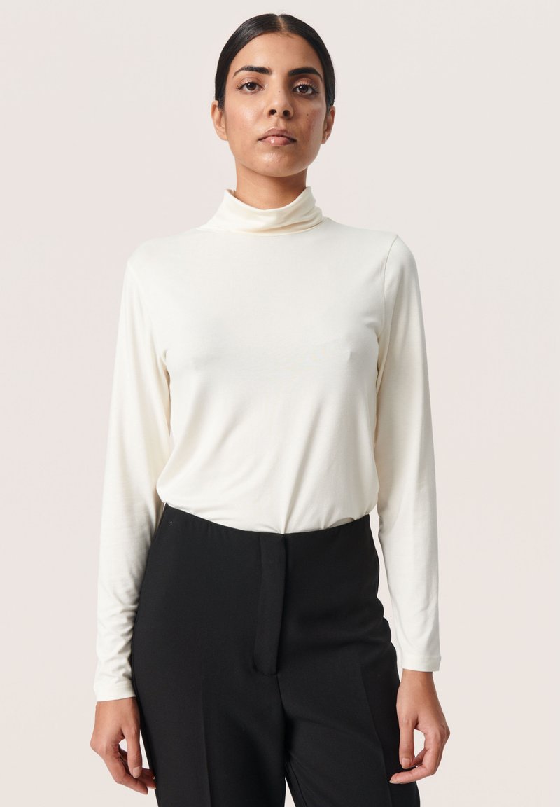 Lange mouw crèmekleurige coltrui met een slimfit ontwerp, zachte textuur en minimale naden, gecombineerd met hoge zwarte slim-fit broek.