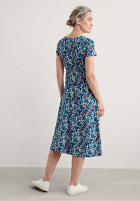 Floral dress with short sleeves, blue and purple patterns, mid-length, soft fabric, worn with white sneakers, viewed from the back.