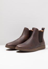 Botas Chelsea de cuero marrón con laterales elásticos, puntera redondeada, superficie texturizada y suela de goma contrastante. Diseño minimalista.