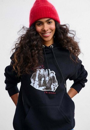 Czarna bluza z kapturem i kieszenią typu kangurka, z grafiką przedstawiającą sześć postaci z serialu w czerni i bieli, z czerwonymi napisami jako akcentem. Czerwona dziana czapka zimowa.