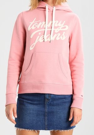 Różowa bluza z kapturem z białym logiem "tommy jeans", z regulowanym kapturem, przednia kieszeń typu kangur oraz ściągacze przy rękawach, zestawiona z dżinsową spódnicą.