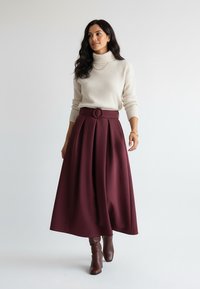 Kremowy prążkowany sweter z golfem w połączeniu z bordową spódnicą midi o linii A z okrągłym paskiem oraz brązowymi kozakami za kolano.