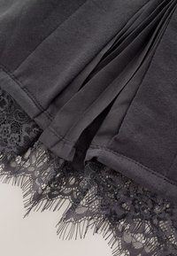 Tissu noir avec plis et bordure en dentelle florale détaillée le long du bord, montrant la texture et les coutures en gros plan.