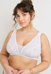 Bralette bianco in pizzo con design a V, motivo floreale e spalline larghe. Presenta una fodera liscia sotto, offrendo comfort e supporto.
