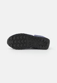 Saucony løpesko med en teksturert svart gummiyttersåle, utstyrt med triangulære pigger for grep og lilla detaljer på overdelen.