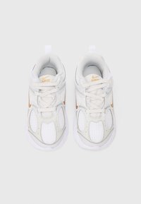 O pereche de adidași Nike albi și bej pentru alergare, cu panouri din plasă și sfori, văzuți de sus pe un fundal simplu.