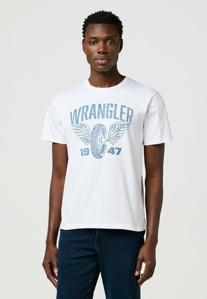 Hvid bomulds t-shirt med blå "WRANGLER" grafik med vinger og året "1947." Standard rund halsudskæring og korte ærmer.