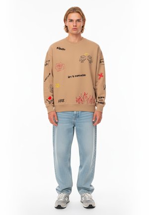 Felpa beige con vari design grafici, tra cui rose e fiamme. Abbinata a jeans blu chiaro a gamba dritta e sneakers grigie sportive.