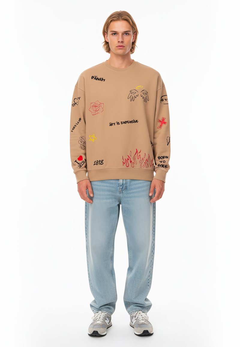 Felpa beige con vari design grafici, tra cui rose e fiamme. Abbinata a jeans blu chiaro a gamba dritta e sneakers grigie sportive.