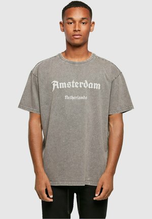 Grå oversized t-skjorte laget av bomull, med "Amsterdam" i hvit gotisk skrift over brystet. Rund hals, korte ermer.