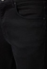 Zbliżenie na czarne dżinsy, ukazujące kieszeń przednią, szlufkę na pasek, guzik oraz detale szycia.