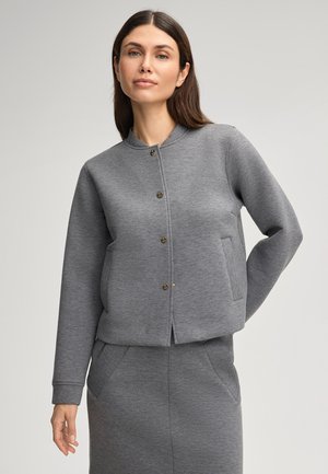 Grijze sweatshirt van zacht materiaal, met een ronde kraag, sluiting met knopen aan de voorkant en zijzakken. Gladde textuur met een getailleerd ontwerp.