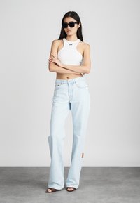 Top sin mangas blanco con el logo "OFF", jeans de pierna ancha azul claro con costuras visibles, gafas de sol negras y sandalias de tacón marrones.