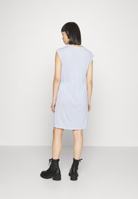 Vestido azul claro de manga curta com cintura franzida. A modelo combina-o com botins pretos de atacadores, exibindo um visual descontraído e relaxado.
