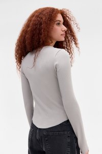 Lys grå langermet topp med ribbet tekstur, avrundet kant og figurnær passform. Kombinert med mørkegrå høyt liv jeans.
