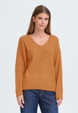 Pull en tricot côtelé, col en V, de couleur orange chaud. Il a des manches longues, une coupe décontractée et une surface texturée. Associé à un jean bleu foncé.