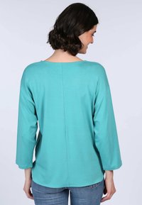 Türkiser Langarmshirt in lockerer Passform, mit einem weiten Ausschnitt, überschnittenen Schultern und einem dezenten Nahtdetail auf der Rückseite.