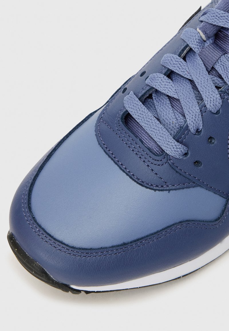 Marineblå lædersneaker med struktureret overflade, rund tå og åndbare lufthuller. Har flade snørebånd og en sort gummisål.