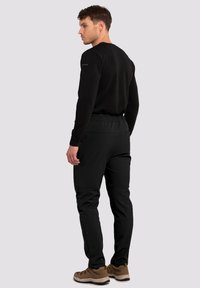Sorte træningsbukser med elastisk talje, tapered fit og sidelommer, båret med en sort langærmet top og brune vandresko.